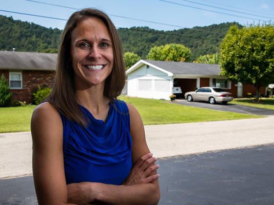 Female researcher standing with arms crossed in front of a house.